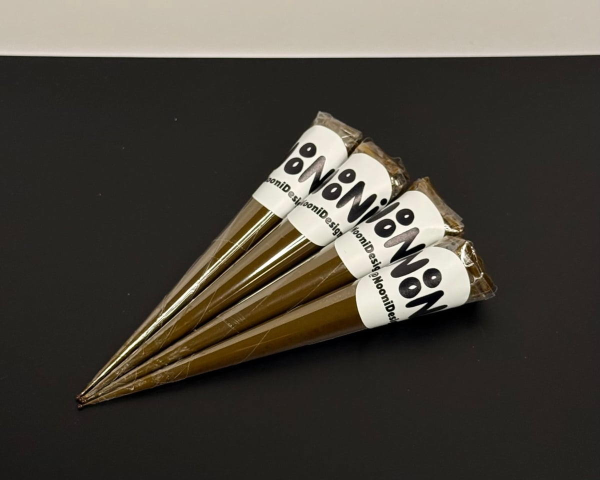 Four NooniDesigns henna cones fanned out together on a dark surface, each wrapped in a white sticker showing the NoNi logo.