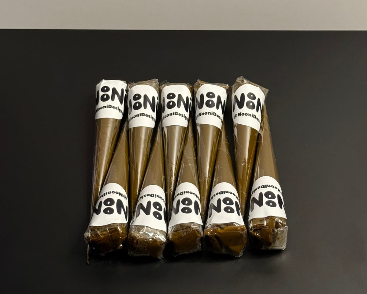 Five NooniDesigns henna cones lined up neatly in a row on a dark surface, each labelled with a white NoNi sticker — typical of a custom event bundle.